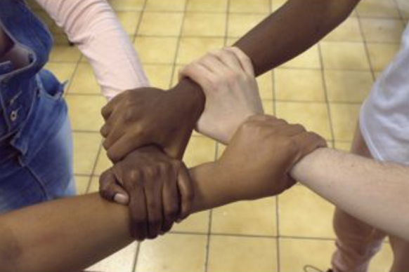 Diverse hands clasping each other in a circle, symbolizing unity and teamwork among people living with disabilities.