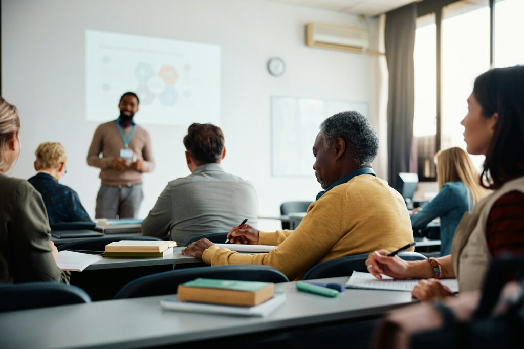 Black senior student man writing while attending adult education class in lecture hall.