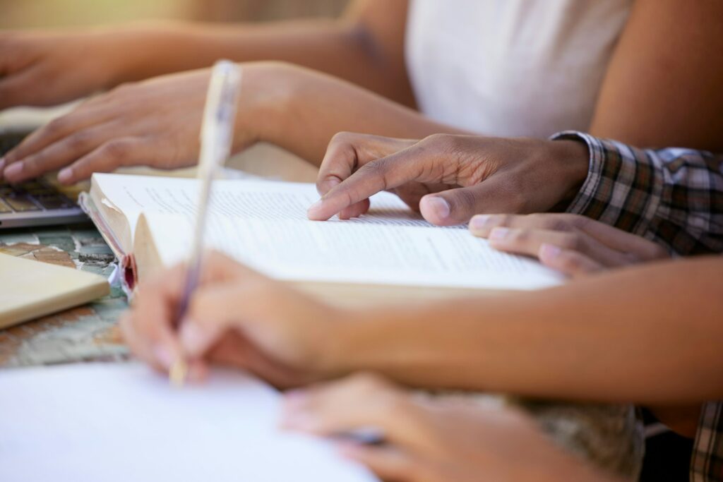Students, education and hands writing in notebook for learning, exam studying and write notes in cl