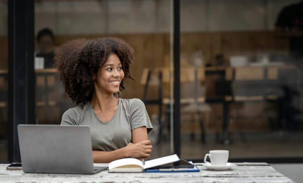 cheerful black woman looking away sitting at desk in cafe. Positive thinking person concept