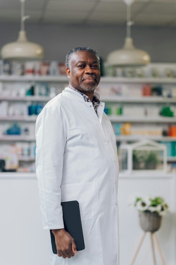 Portrait of a confident male senior multicultural pharmacist holding a tablet while smiling