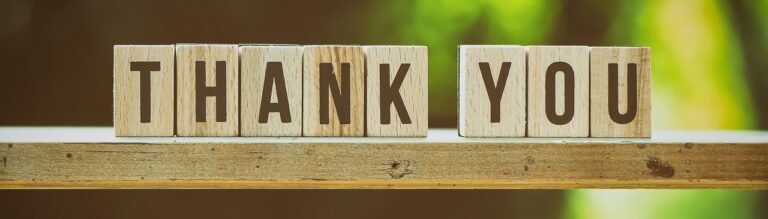 Wooden blocks spelling out "THANK YOU" on a wooden surface with a blurred green background.