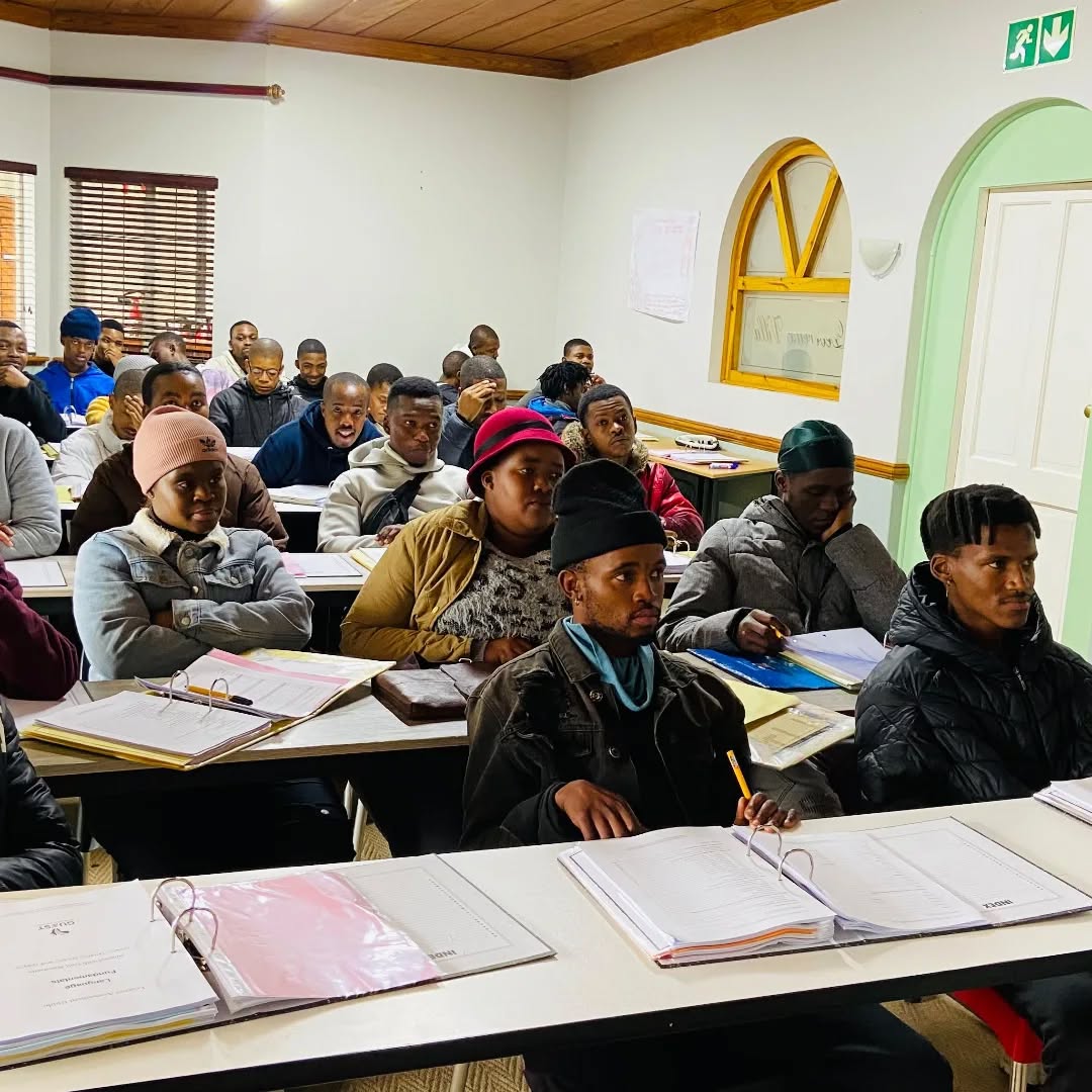 A classroom of students sitting at desks with notebooks and binders, attentively facing forward during a lesson.