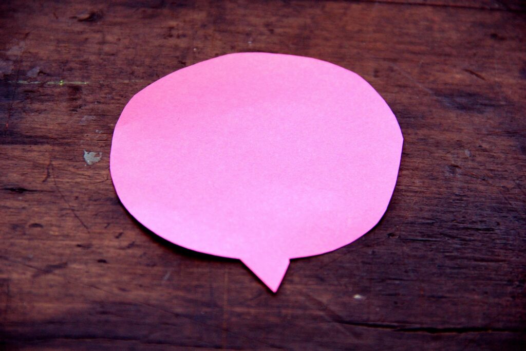 A pink paper speech bubble cutout sits on a dark wooden surface.