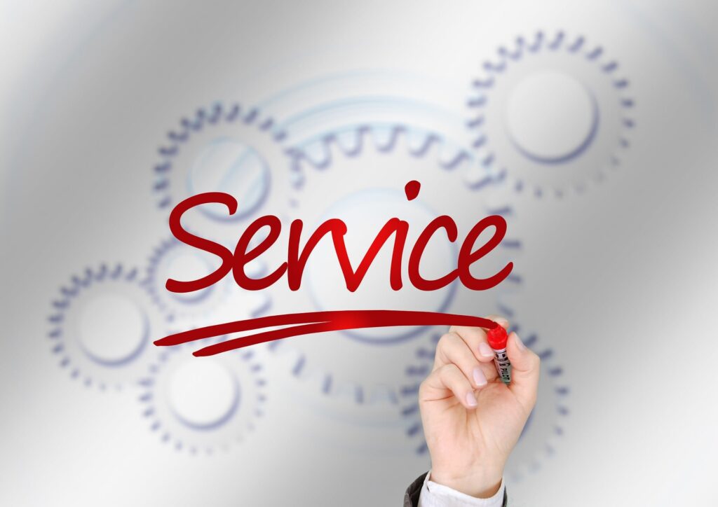 A hand holding a red marker writes the word “Service” in cursive on a transparent surface, with blurred gear graphics in the background.