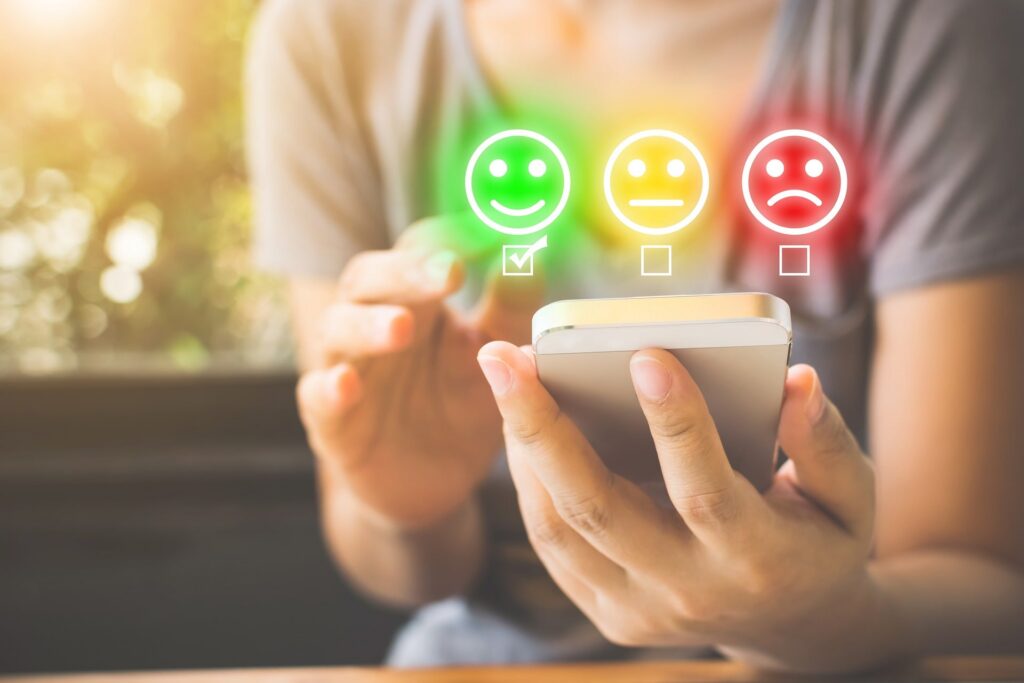Person using a smartphone selects a happy face emoji from three feedback options, representing positive, neutral, and negative choices, with a green checkmark on the smiley face.