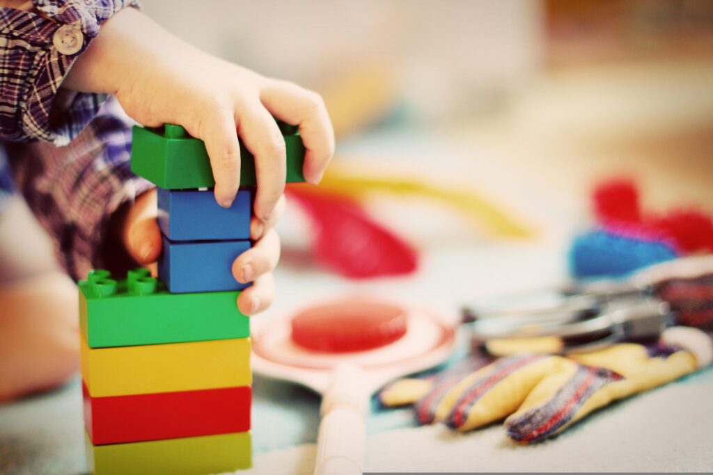 A child’s hand stacking colorful plastic building blocks.